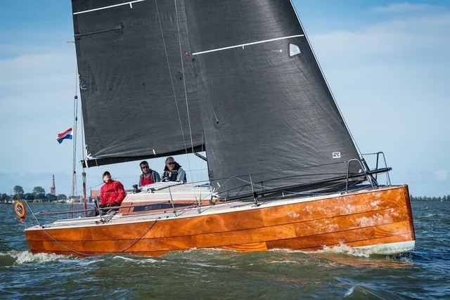 Varnished wood-epoxy Waarschip 1012 sailing upwind under black mainsail and genoa with three crew aboard