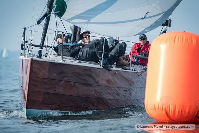 Crew hiking on the varnished wooden rail of the Waarschip 1012 as she passes an orange inflatable mark