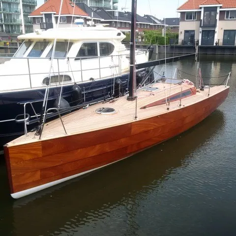 Bright-finished wooden Waarschip 1012 moored bare-masted in a marina beside a dark blue motor yacht