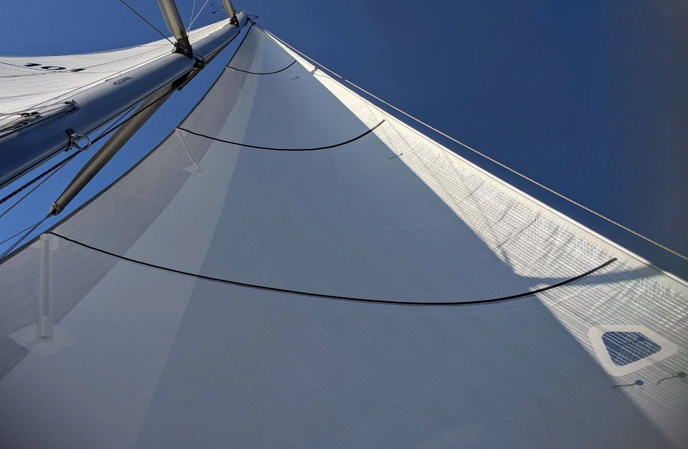 Looking up a white X-Drive® Endure jib with curved load-path tapes, mast and mainsail to the left, blue sky