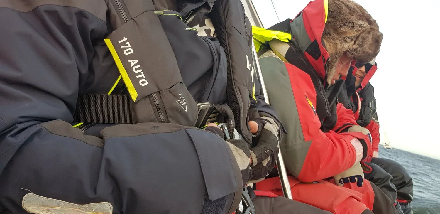 Crew in foul-weather gear and auto-inflate lifejackets huddled on the rail, heads down against the weather