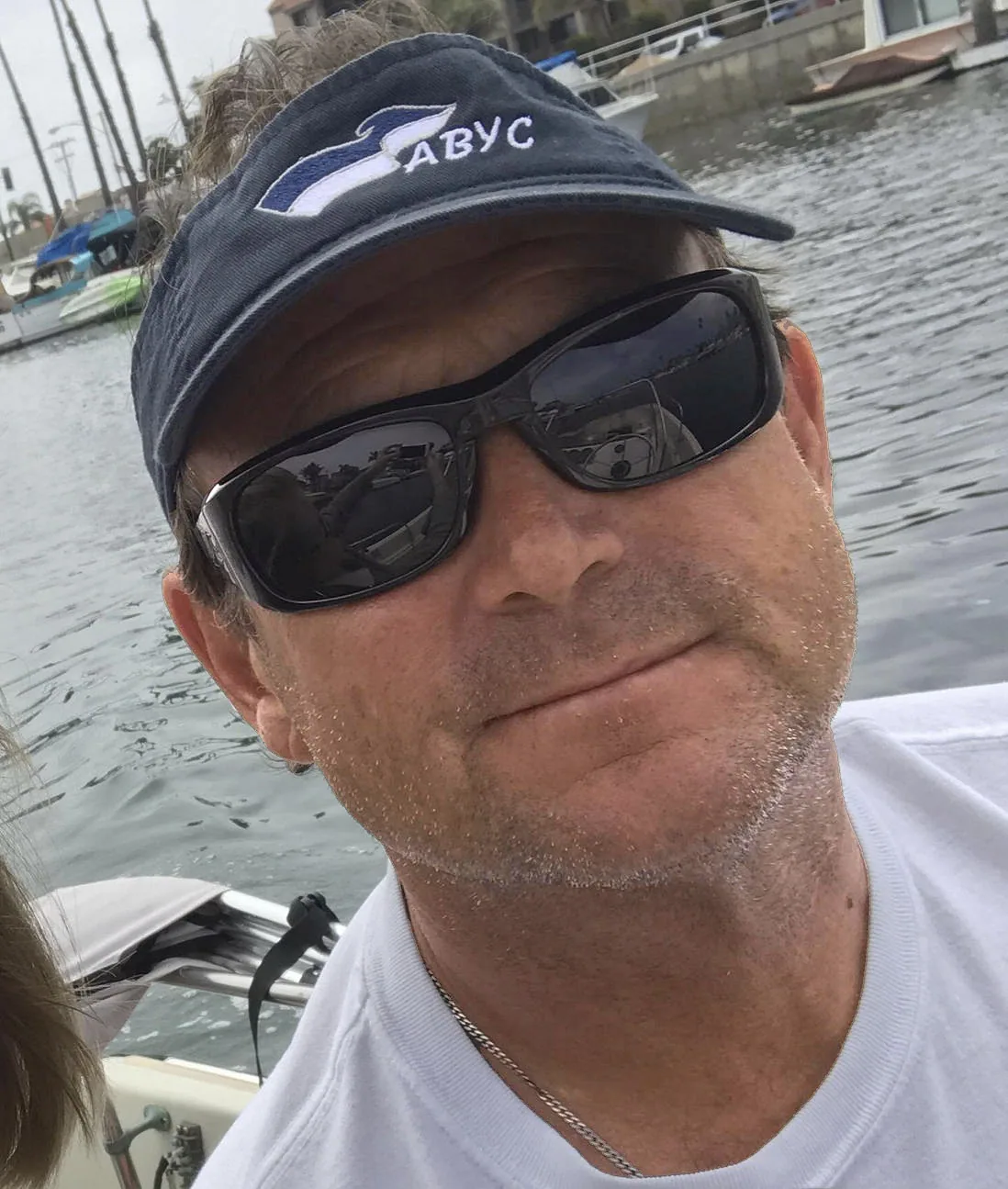 Jim Lincoln smiling in a navy ABYC visor and dark sunglasses aboard a boat in a marina