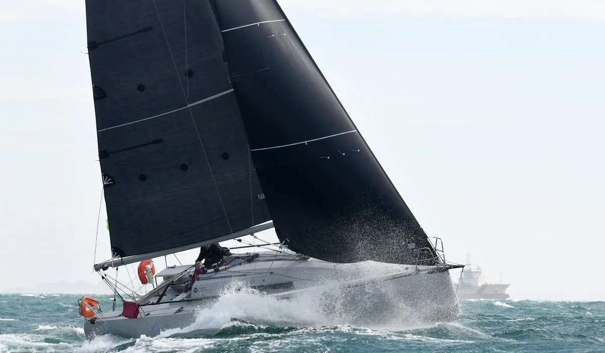 Grey-hulled yacht driving through choppy seas under black mainsail and jib, spray flying, in the 2019 Fastnet Race