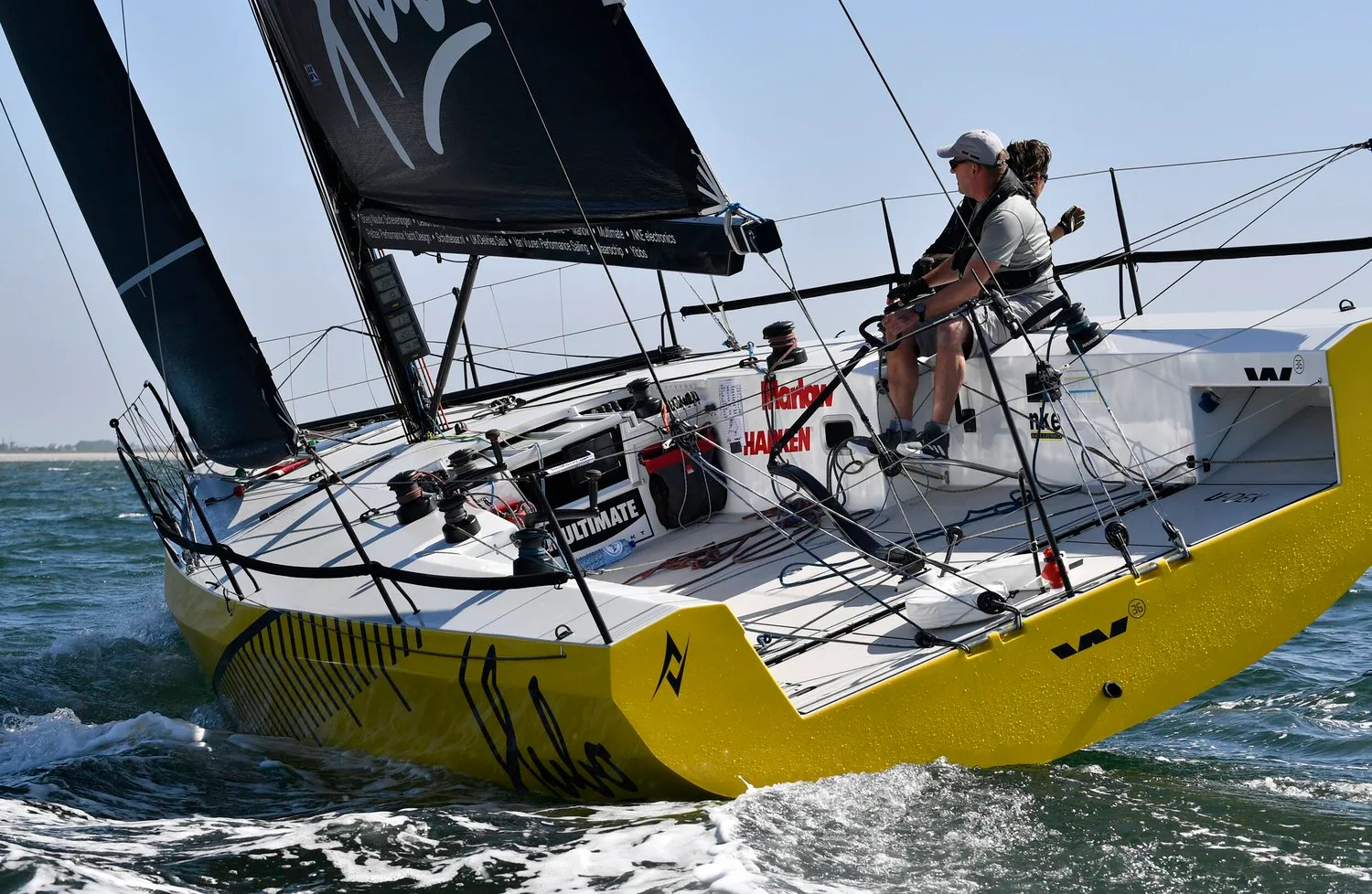 Yellow-hulled HUBO reaching under black mainsail and jib, two crew aft, sponsor lettering on the coachroof