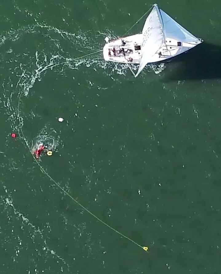 Aerial view of a sailboat circling a swimmer, its trailing LifeSling line curving around the person in the water