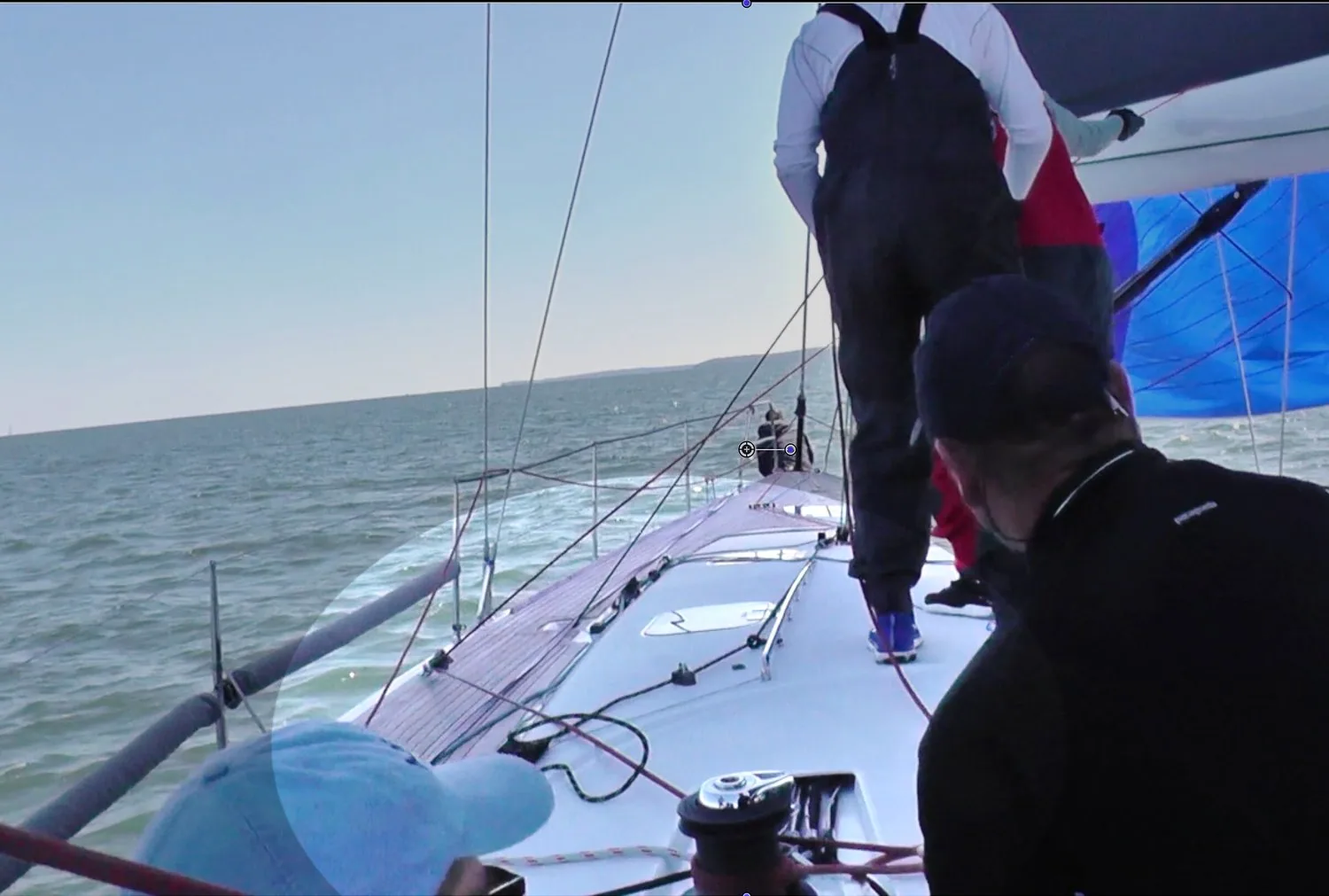 Crew on the side deck of a white racing yacht with a blue spinnaker up and a takedown line led to a block on the rail