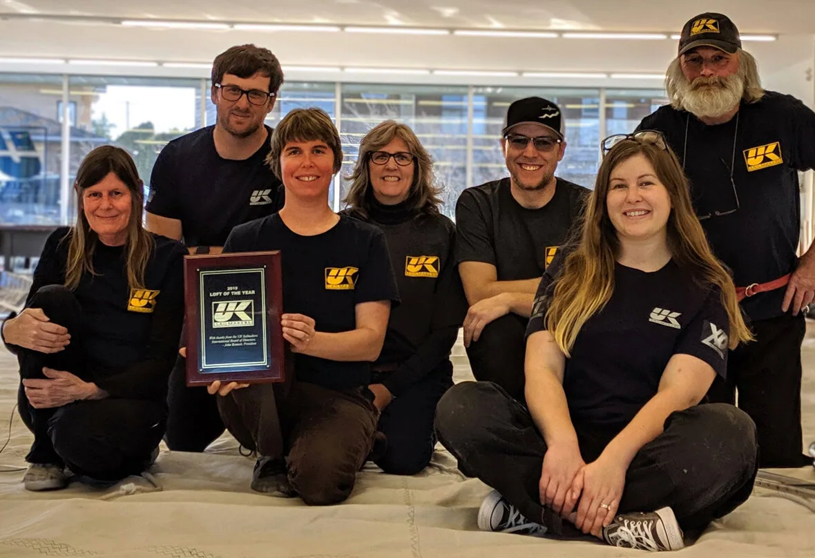 UK Sailmakers Northwest team in black loft T-shirts kneeling on the loft floor with their Loft of the Year plaque