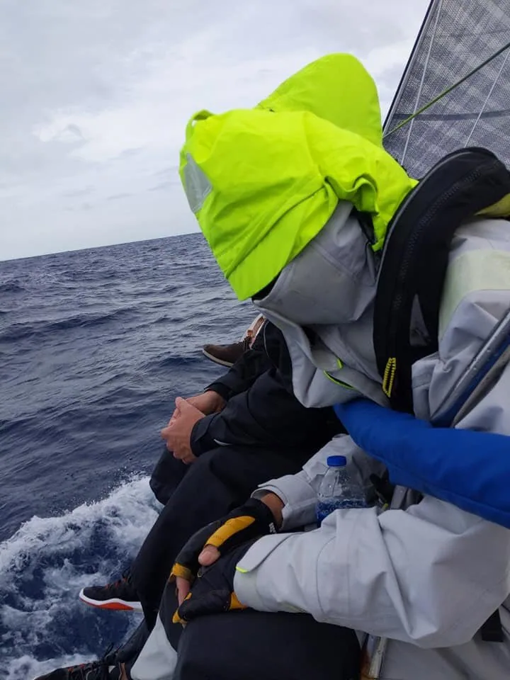 Karen Lewis dozing on KENAI's rail, the yellow hood of her grey foul-weather jacket pulled over her face, grey seas behind