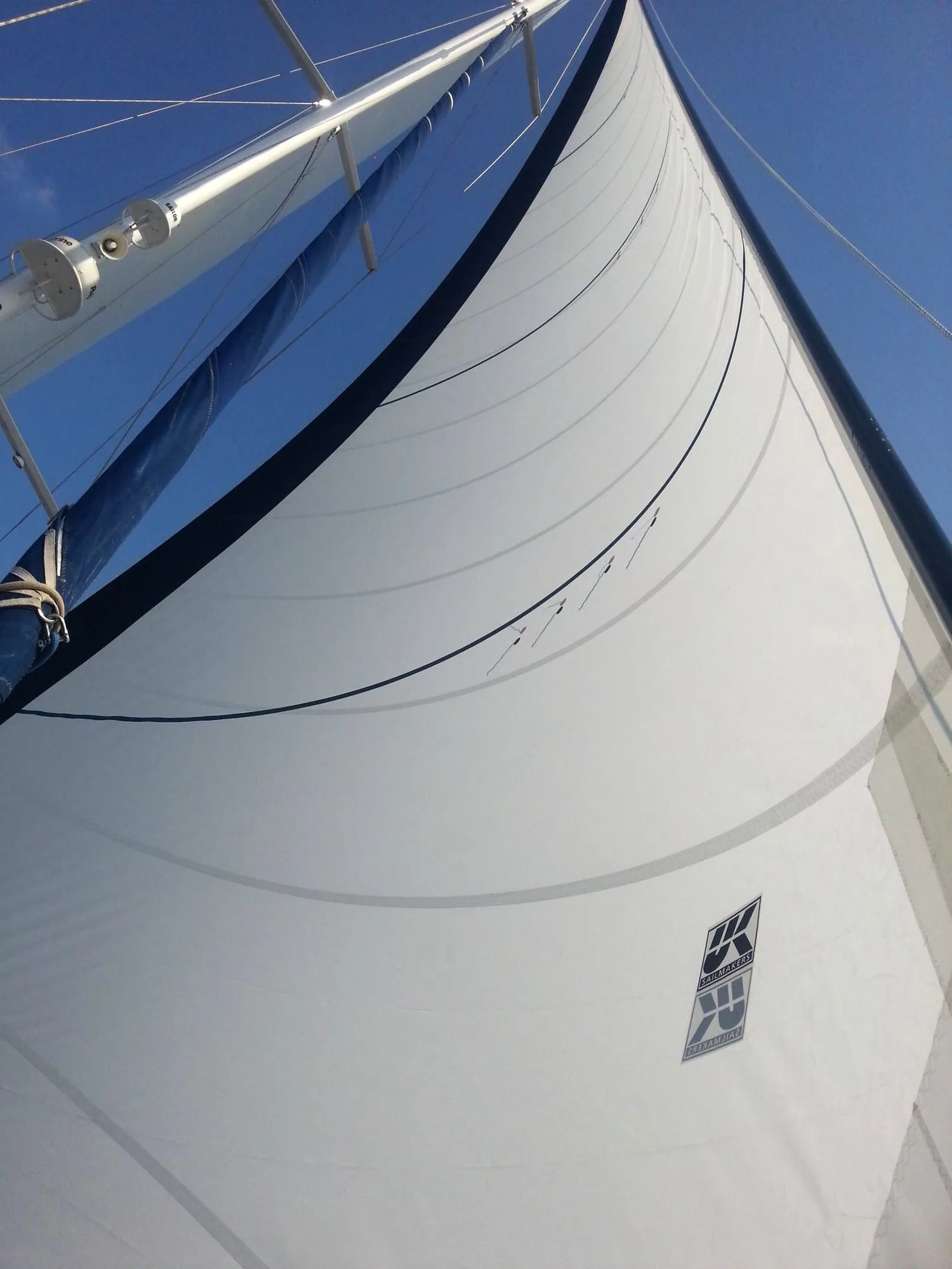 Looking up the luff of a white Dacron genoa with a blue UV cover and UK Sailmakers logo against a blue sky