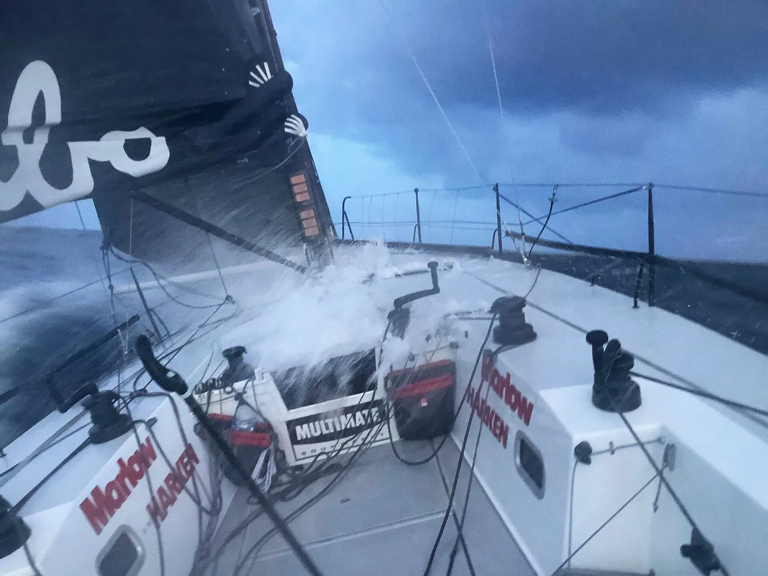 Foredeck awash with spray on the yacht HUBO during the Fastnet Race, grey seas and storm clouds ahead
