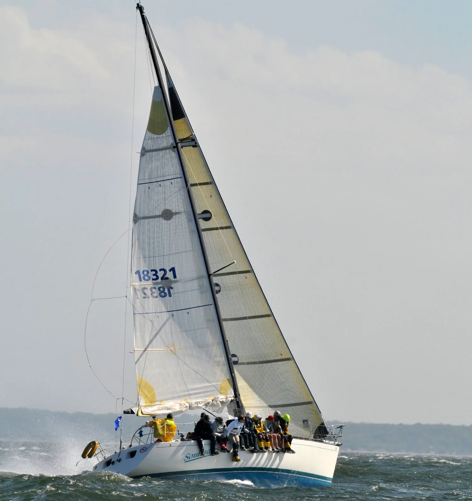 Sloop with sail number 18321 heeled hard to windward under a white laminate main and genoa, crew hiking on the rail