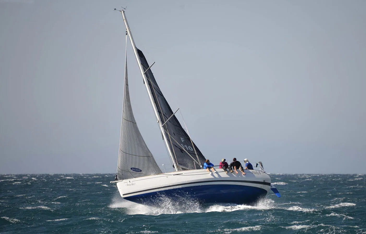 Beneteau First 30 MINKIE punching upwind through steep grey seas under grey laminate main and jib, crew on the rail