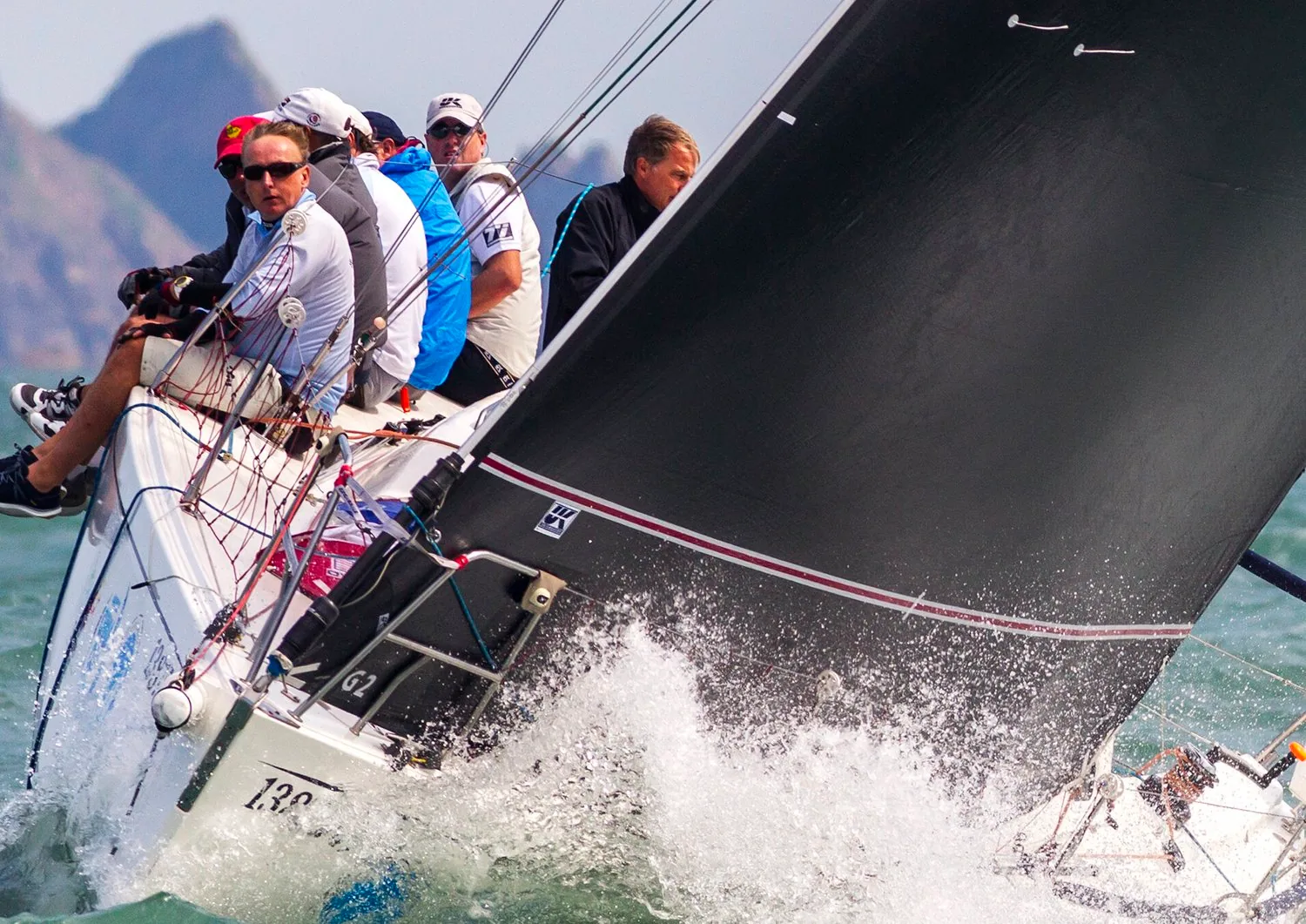 J/109 WHISKEY JACK heeled hard upwind under a black mainsail, crew hiking as spray bursts over the bow