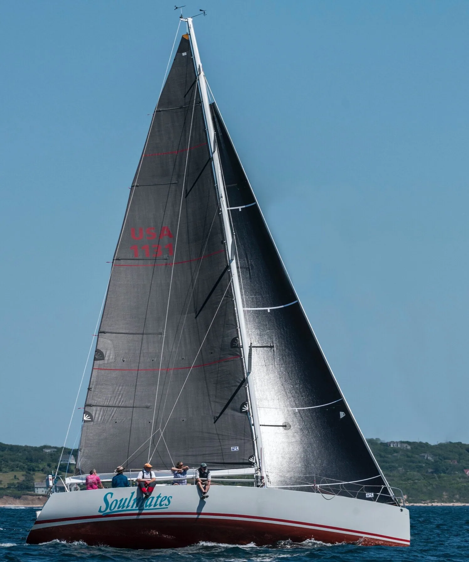 Sloop SOULMATES close-hauled under black carbon main and jib, crew forward on the rail, low green shore behind