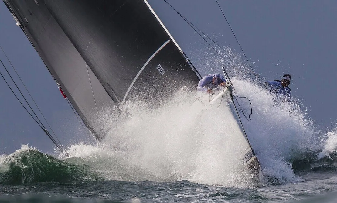 Reichel/Pugh 77 JELIK burying her bow in a wave, spray exploding over the foredeck under black sails