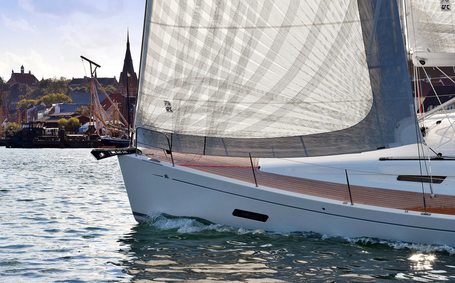 Bow of an Italia 12.98 cruiser under a grey laminate furling genoa, historic waterfront and church spire astern
