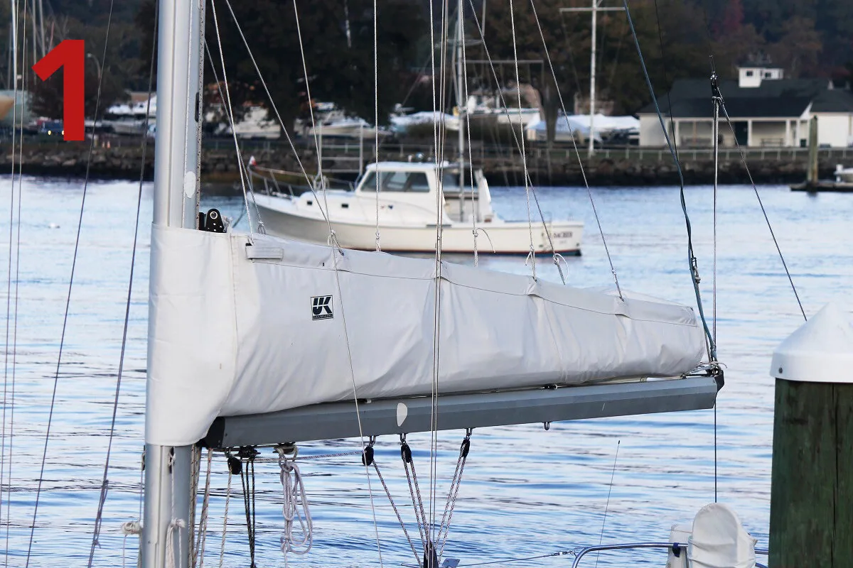 Grey UK Sailmakers lazy cradle mainsail cover zipped along the boom at the dock, labelled 1
