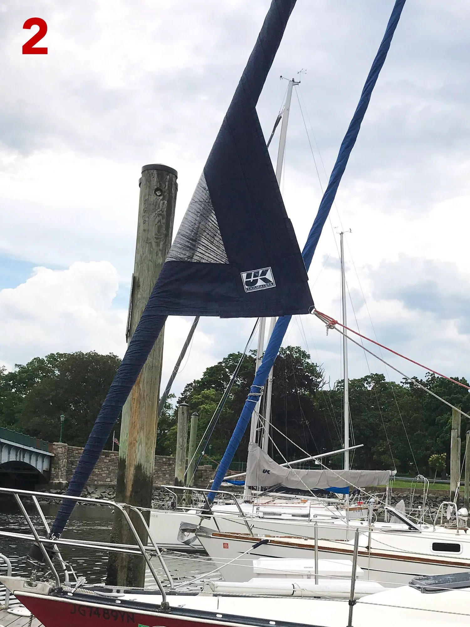 Furled genoa with its dark UV cover stopping short, leaving white sailcloth exposed near the head, labelled 2