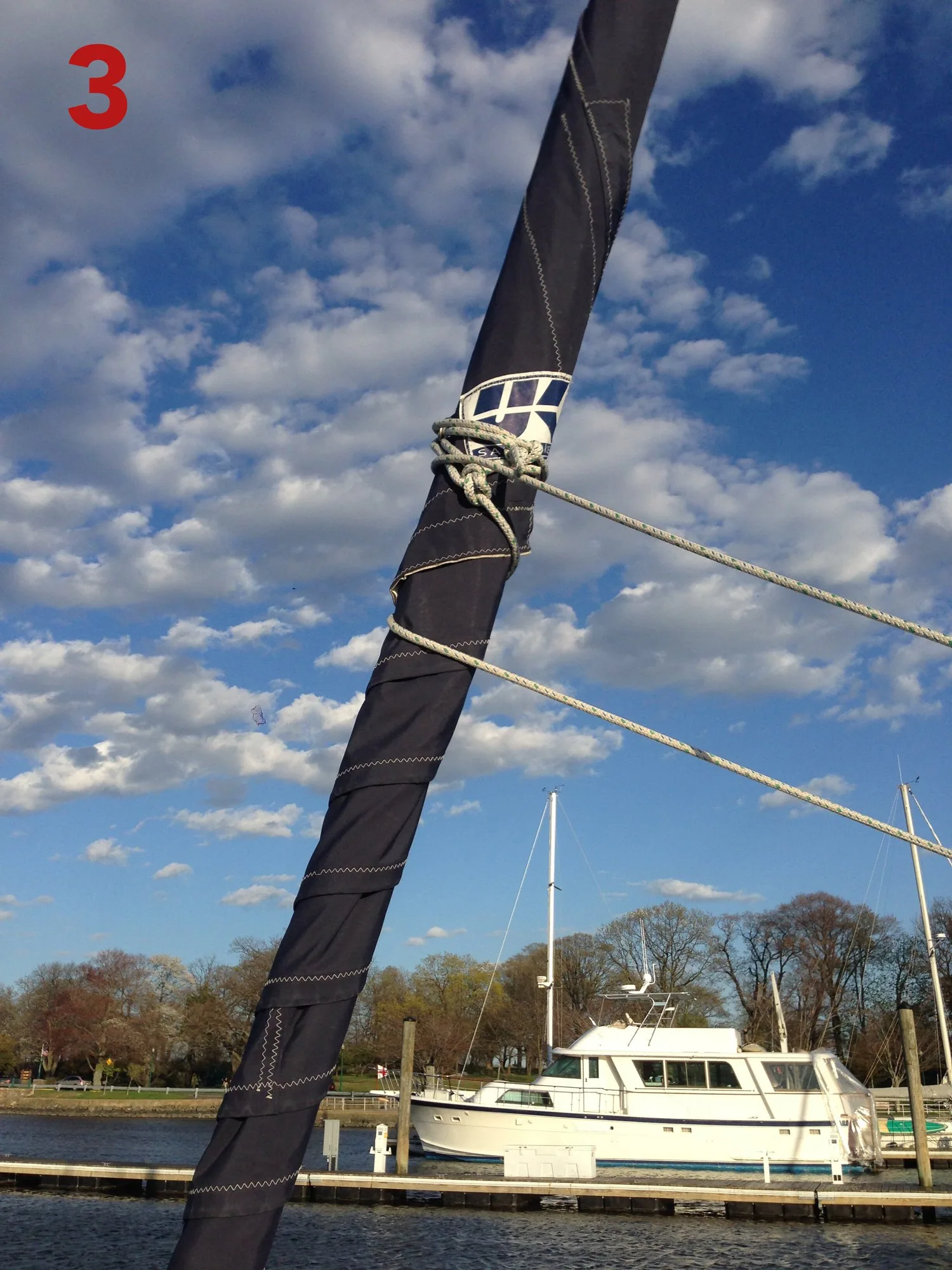 Furled genoa neatly rolled with the dark UV cover fully covering the sail and the sheets wrapped around it, labelled 3