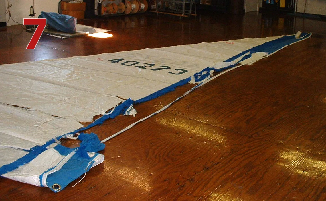 Genoa laid on a loft floor with its blue leech UV cover torn to shreds, sail number 40273, labelled 7
