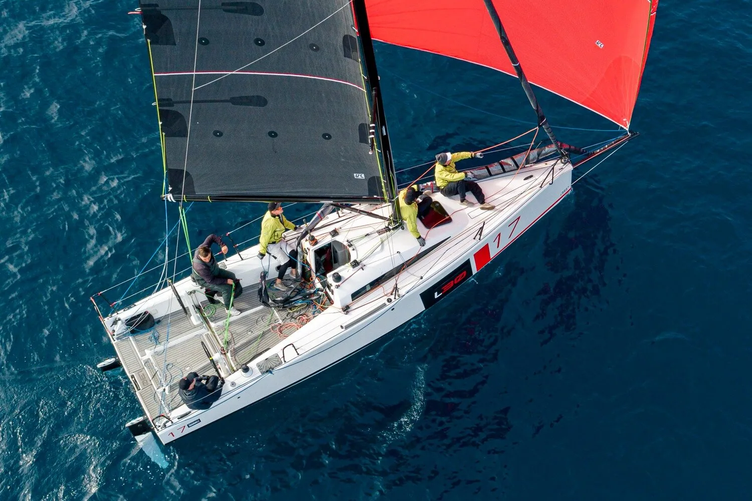 Aerial view of an L30 one-design running under a black mainsail and red asymmetric spinnaker, four crew aboard