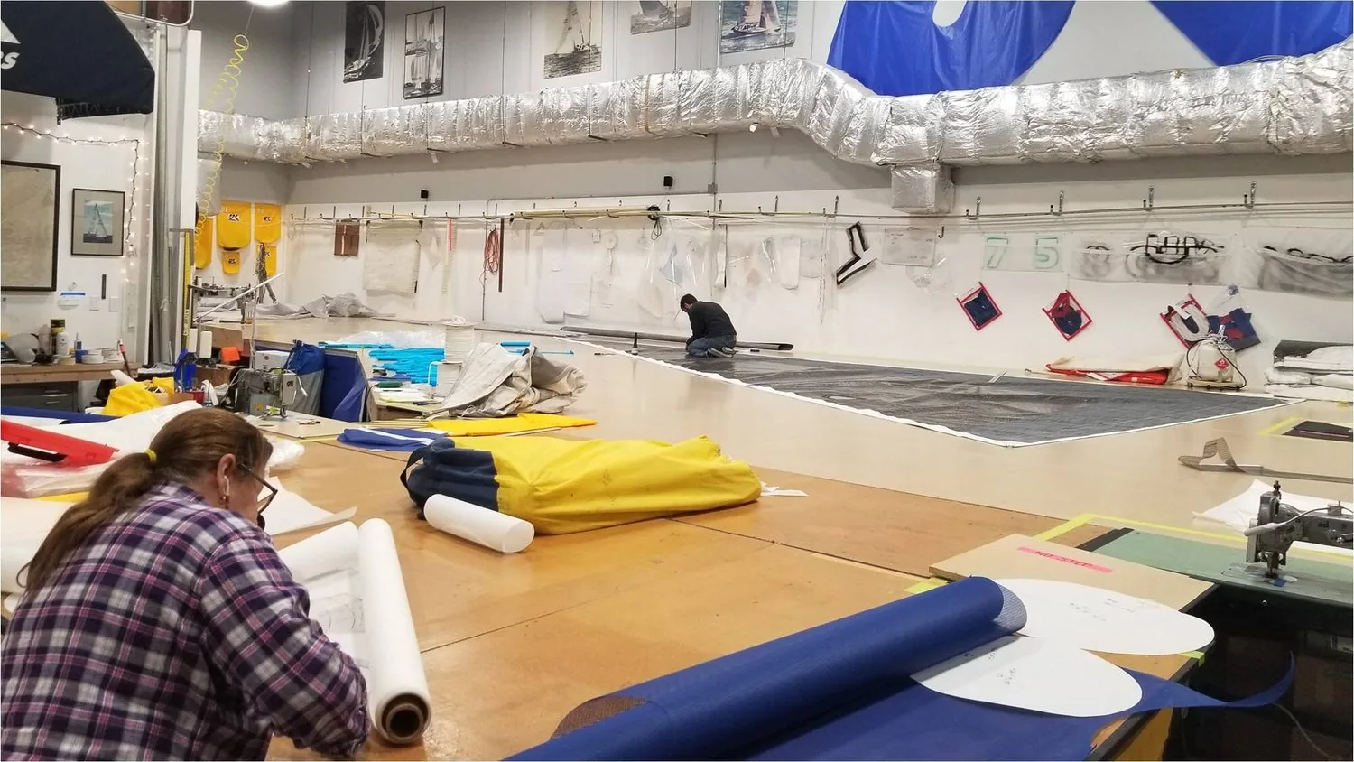 Inside the UK Sailmakers New York loft: a sailmaker at a sewing machine and another kneeling on a long sail on the floor
