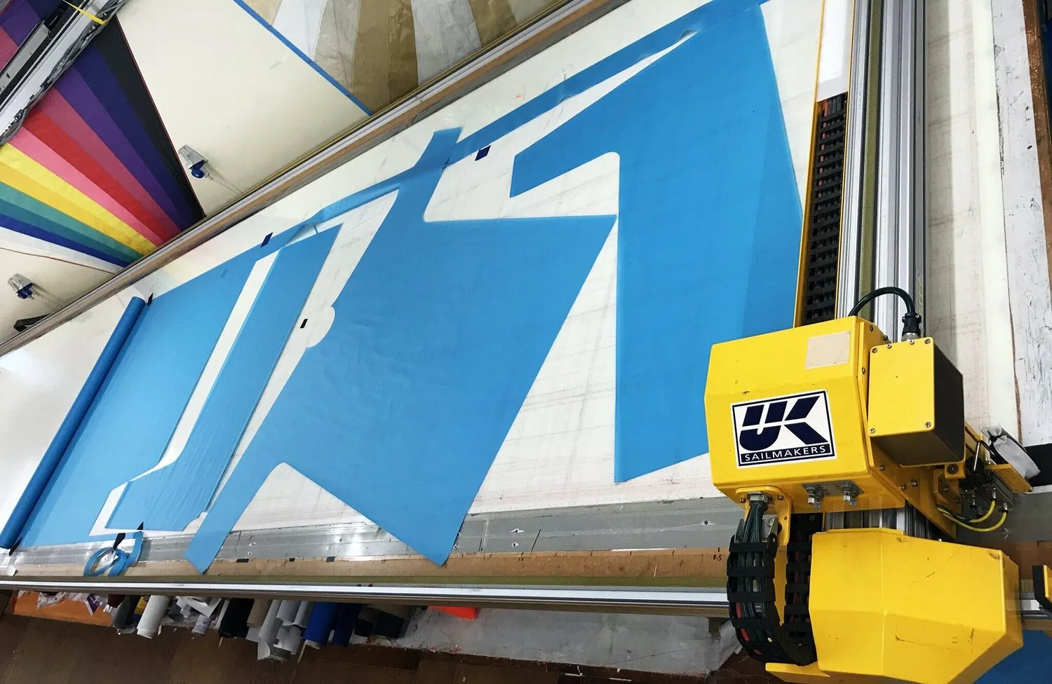 Blue gown panels being cut on the loft plotter table, yellow UK Sailmakers cutter head in the foreground