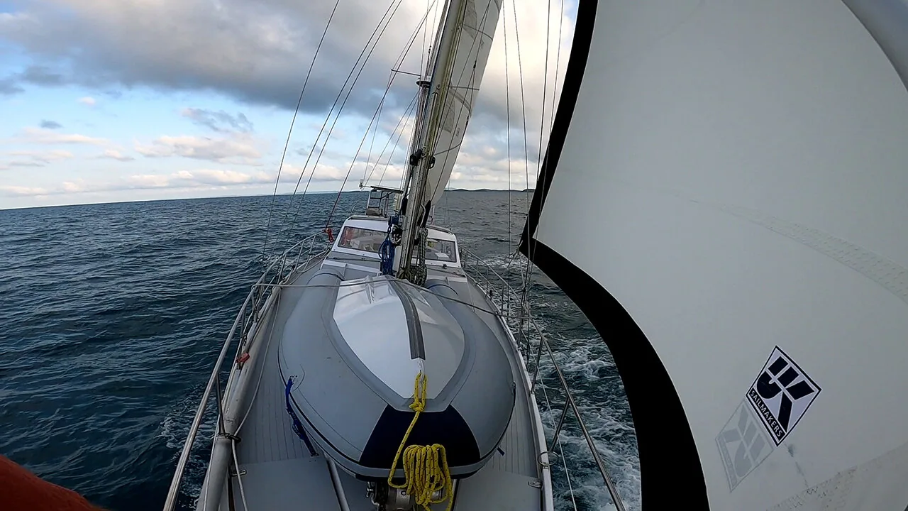 View forward along a cruising sailboat's deck, dinghy lashed on the foredeck, UK Sailmakers headsail drawing