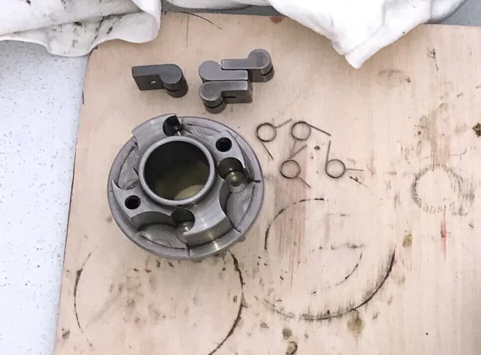 Winch gear hub with its pawls and pawl springs removed and laid out beside it on a plywood board
