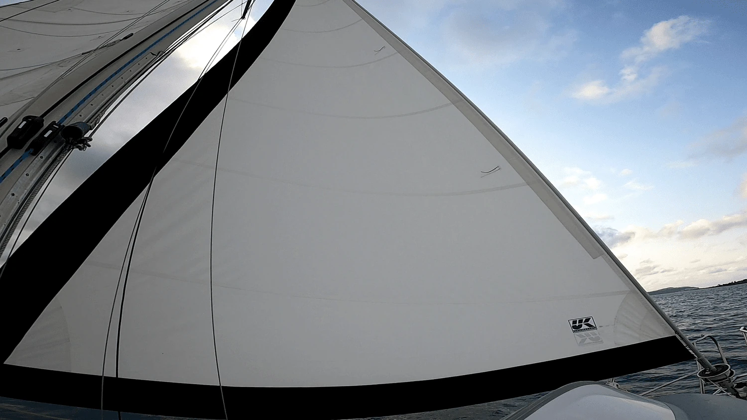 White furling headsail with a black UV strip along the leech and a UK Sailmakers logo, seen from the cockpit