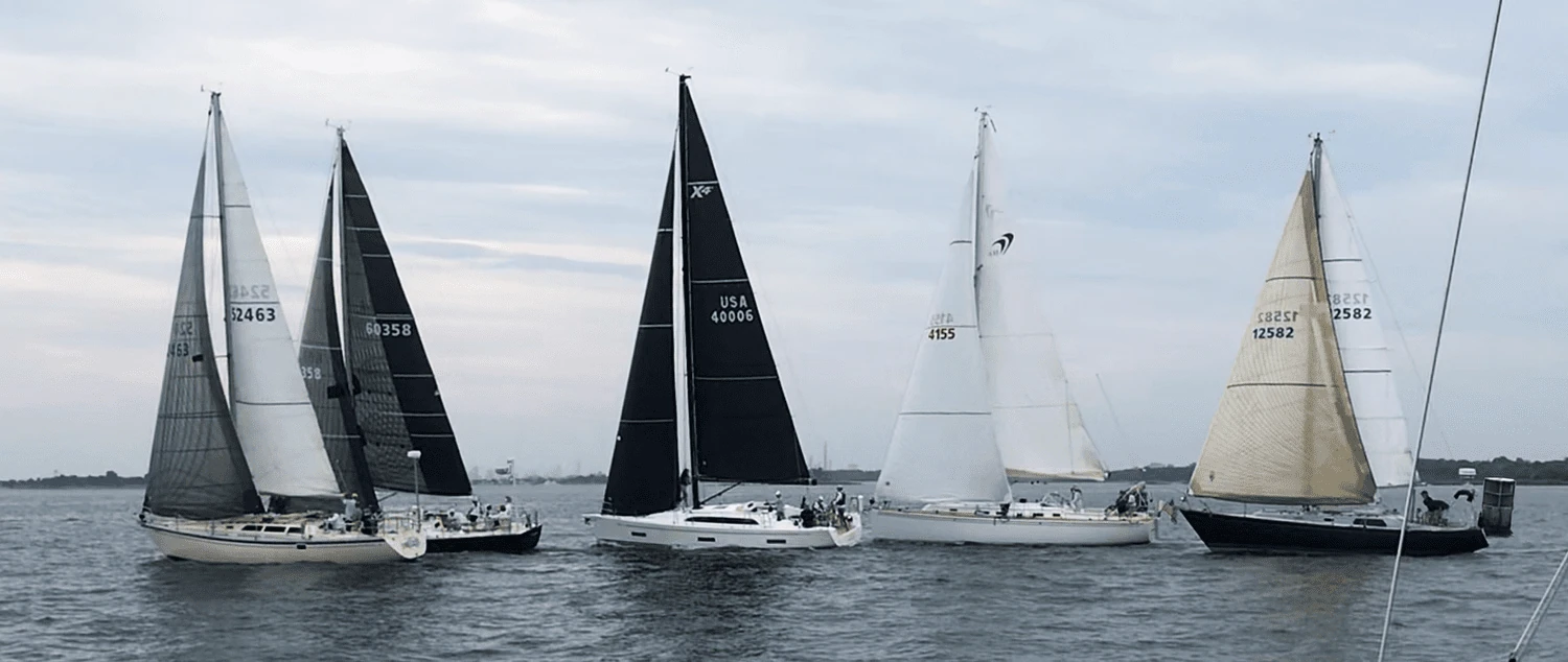 Five cruiser-racers crossing a start line in light air under grey skies, sails barely filled
