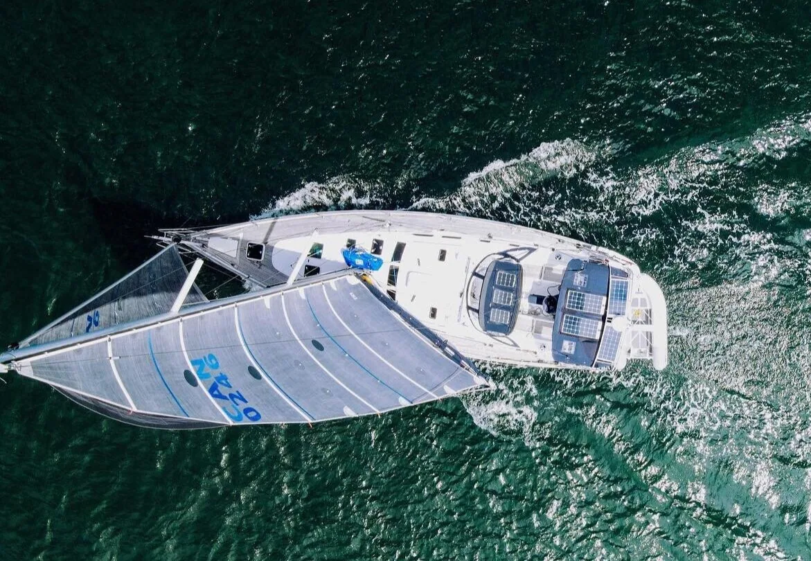 Overhead drone view straight down onto a cruising yacht sailing under a pale blue headsail on green water