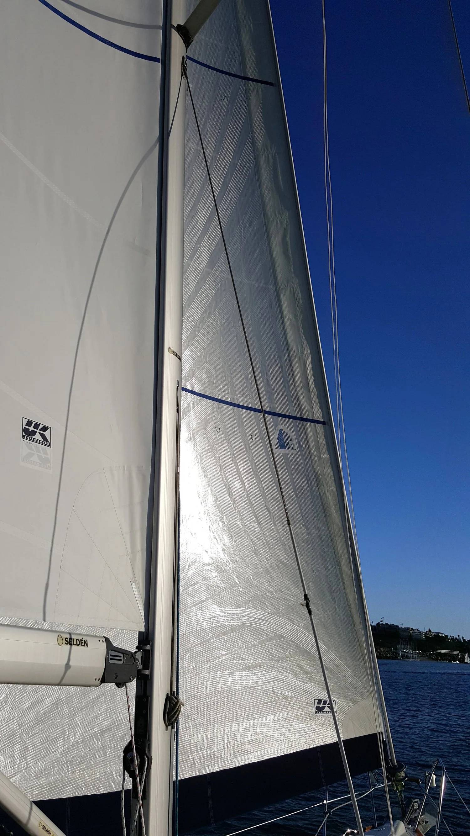Silver-grey laminate main and genoa with blue draft stripes and UK Sailmakers logos, seen from the deck