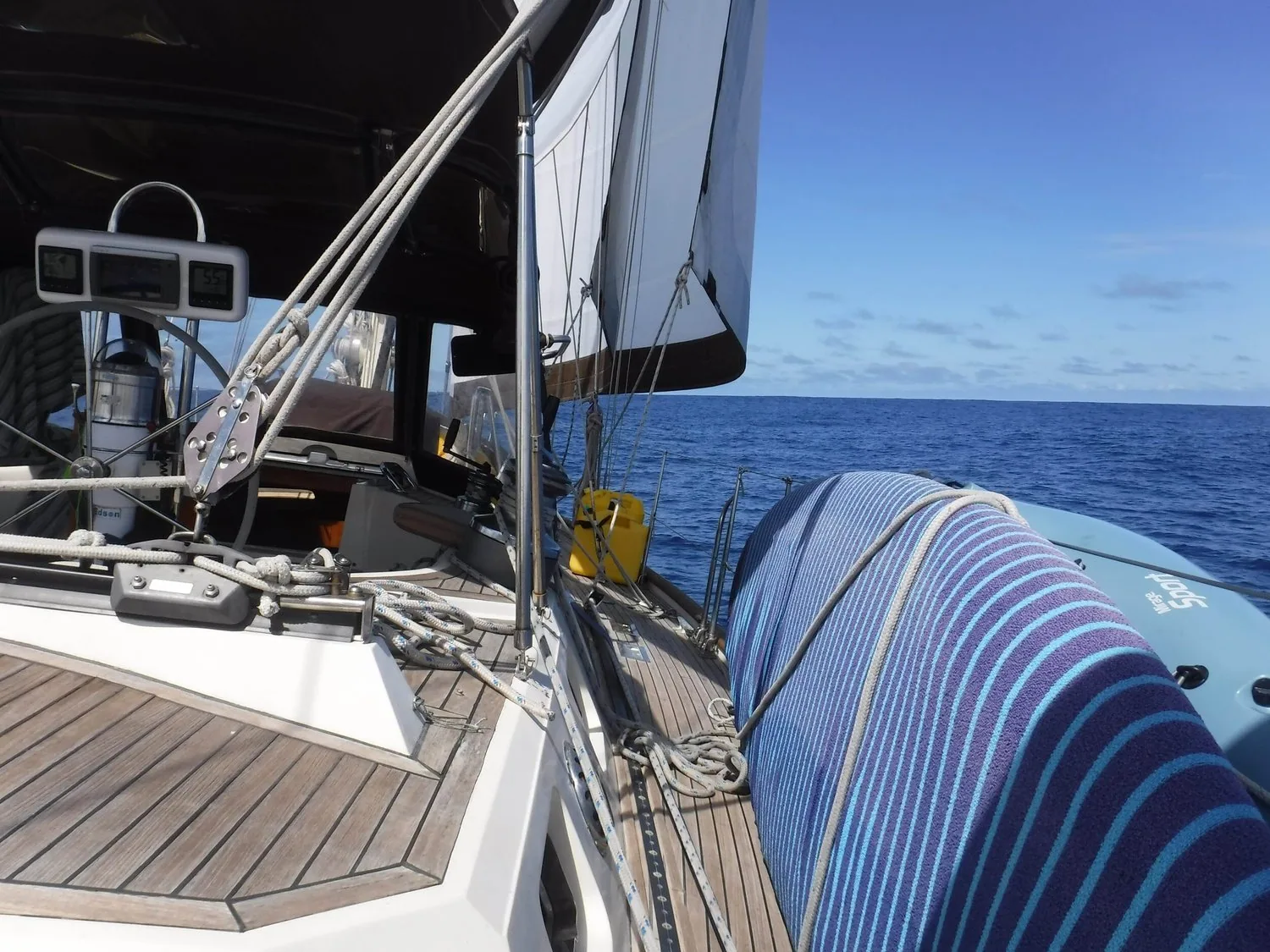 Aboard Silver Heels offshore: teak deck, pole lashed alongside and a blue-and-white striped rolled sail bundle