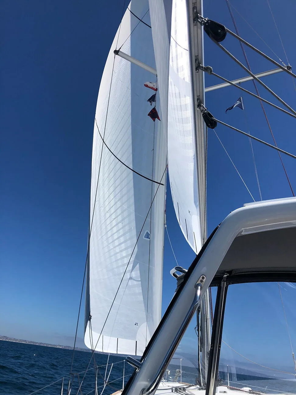 White X-Drive® Endure main and genoa seen from beneath the bimini frame, signal flags hoisted, clear blue sky