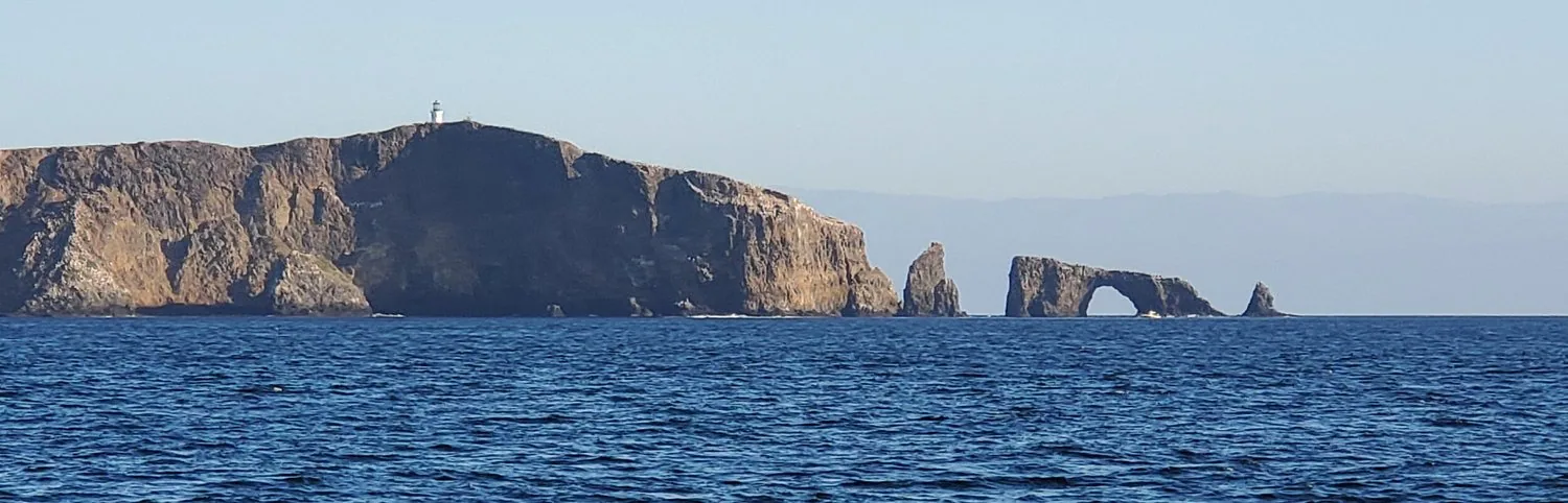 Rocky island headland ending in a natural sea arch, seen from the water in the Channel Islands