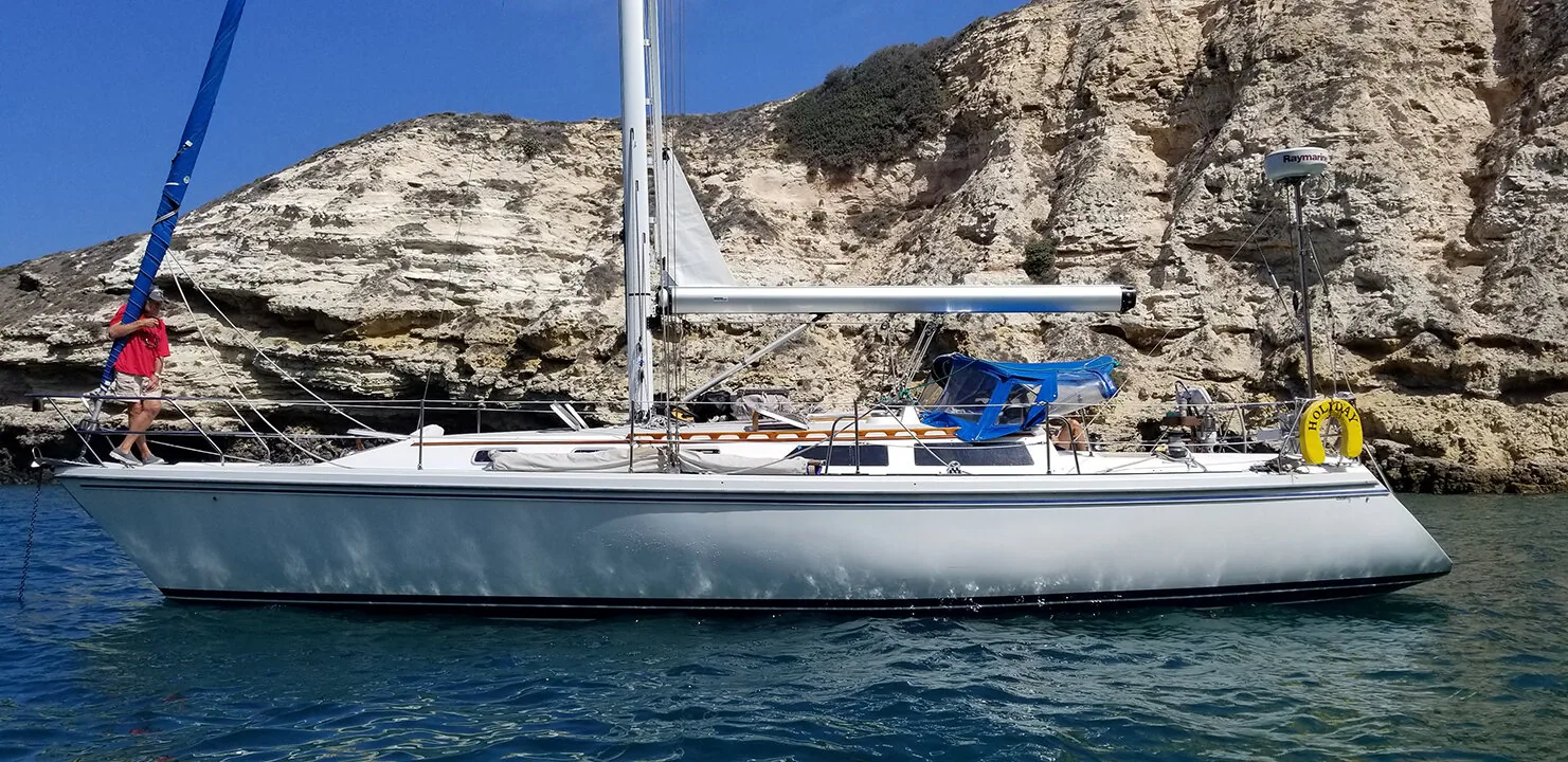 White cruising sloop anchored beneath pale sandstone cliffs, crew member on the bow, Channel Islands