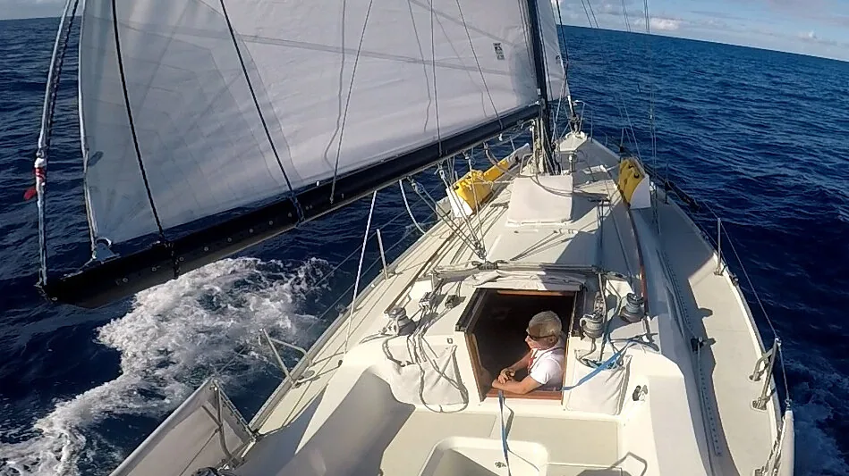 Wide-angle view down the deck of an Ericson 38 under a grey genoa offshore, sailor in the companionway