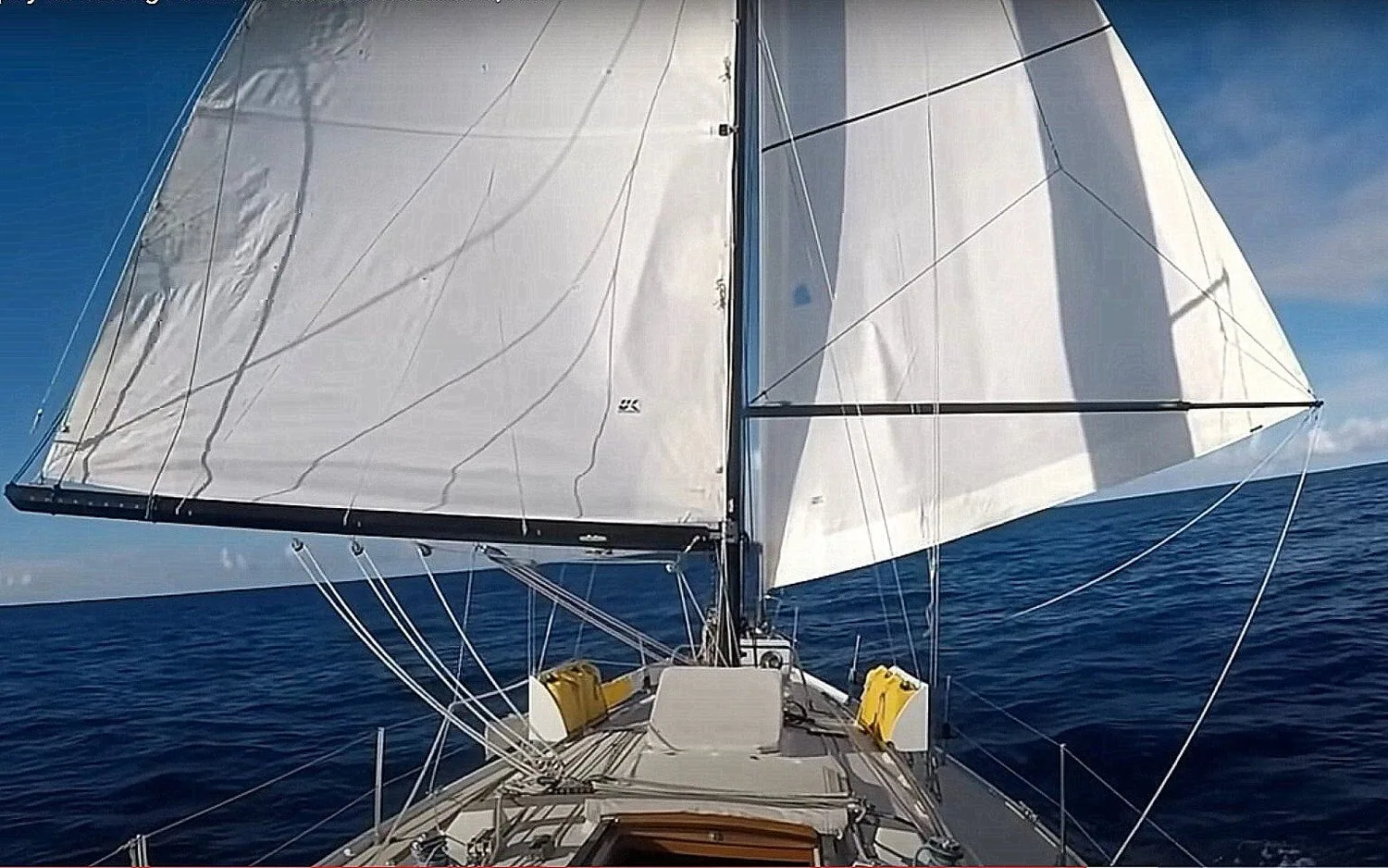 Ericson 38 sailing offshore under full white mainsail and genoa, seen from the cockpit looking forward