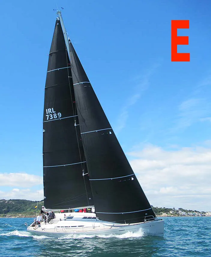 Photo E: Beneteau First 50 sailing under black mainsail and jib, sail number IRL 7389, hills behind