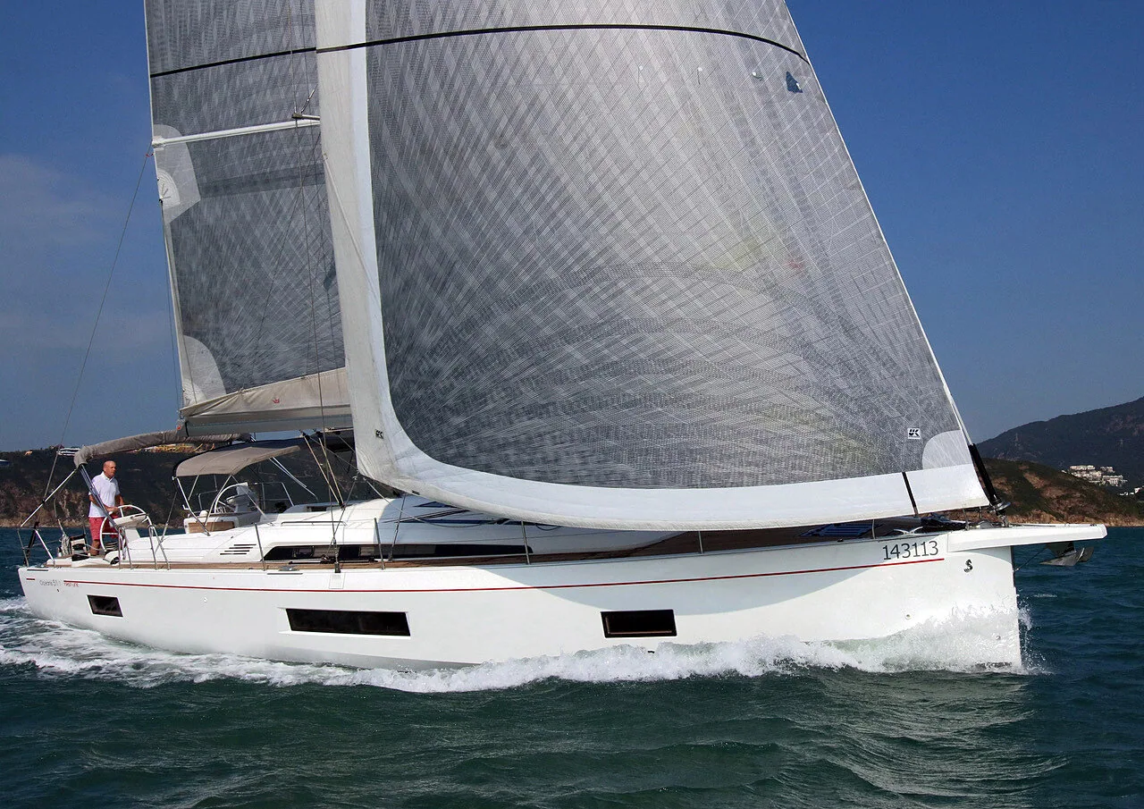 Beneteau Oceanis 51 sailing under grey X-Drive® mainsail and genoa, sail number 143113, green hills behind