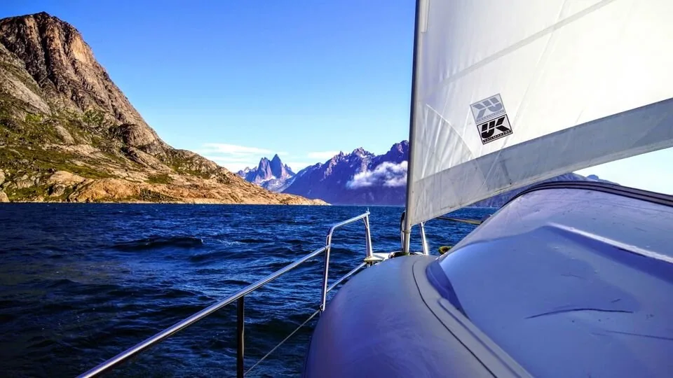 Looking forward past a white UK Sailmakers headsail towards jagged Greenland peaks across a fjord