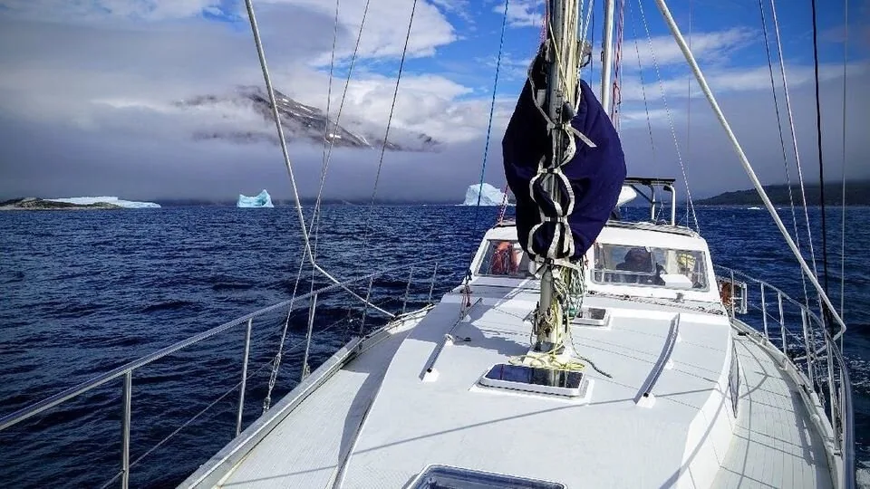 Looking forward along PANDA's deck, an Amel Sharki, towards icebergs and cloud-capped Greenland mountains