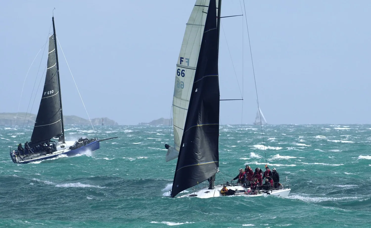 CHECKMATE burying her bow downwind in heavy air under a black mainsail, a second dark-sailed yacht astern