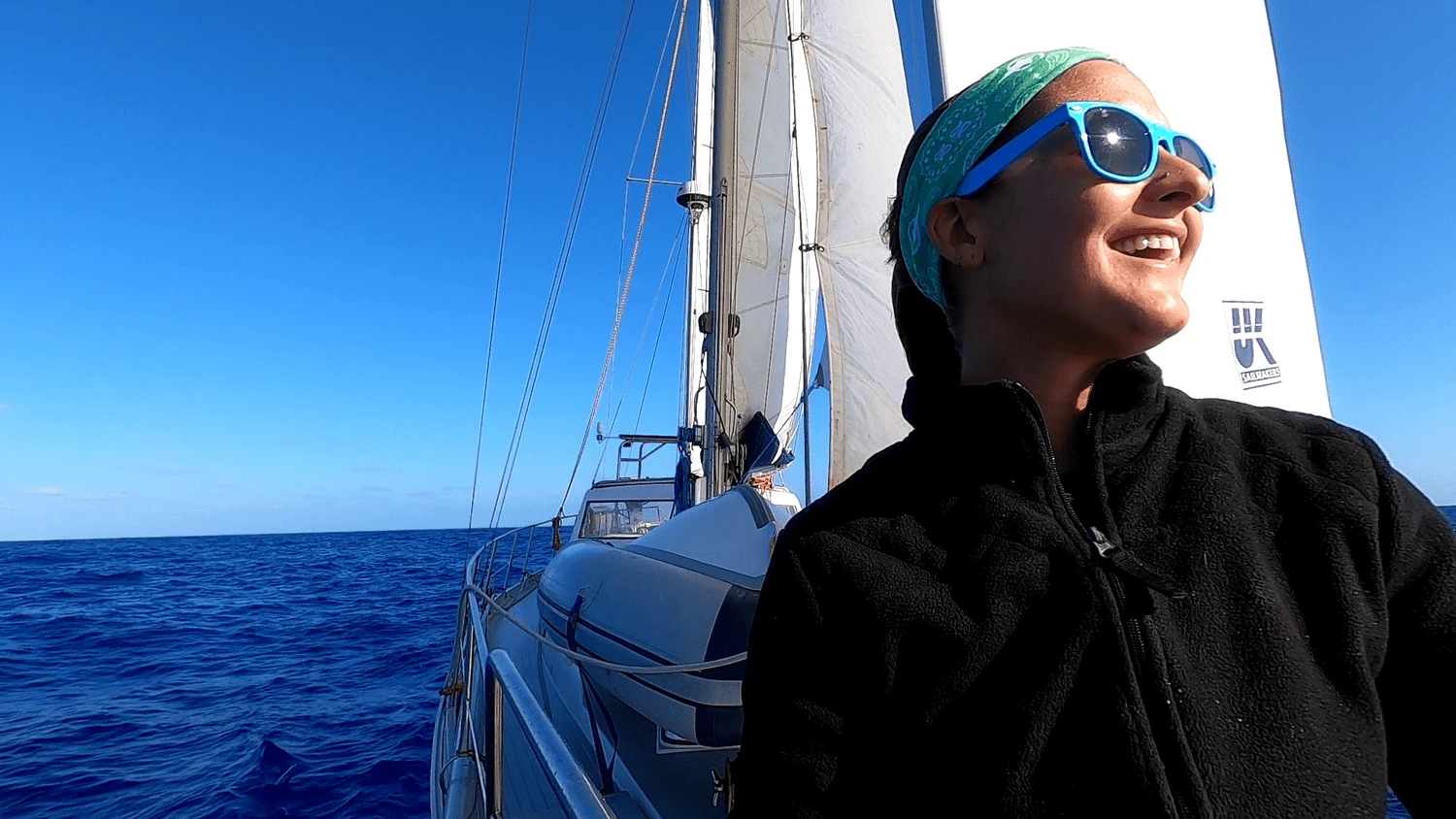 Amanda in a black jacket, turquoise headband and blue sunglasses smiling on PANDA's deck under sail