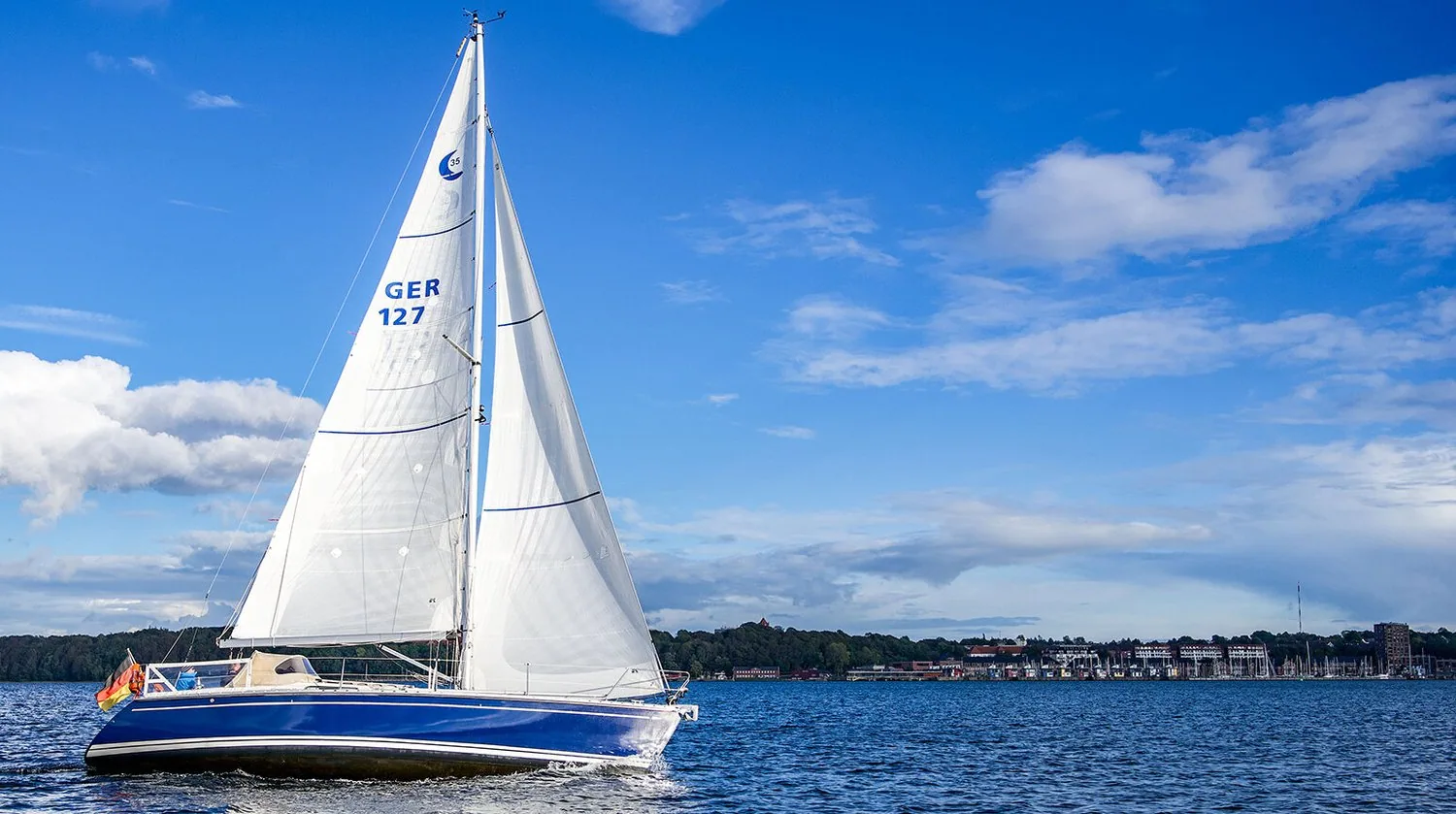 Comfortina 39, GER 127, with a navy hull sailing under white X-Drive® Silver mainsail and genoa past a waterfront
