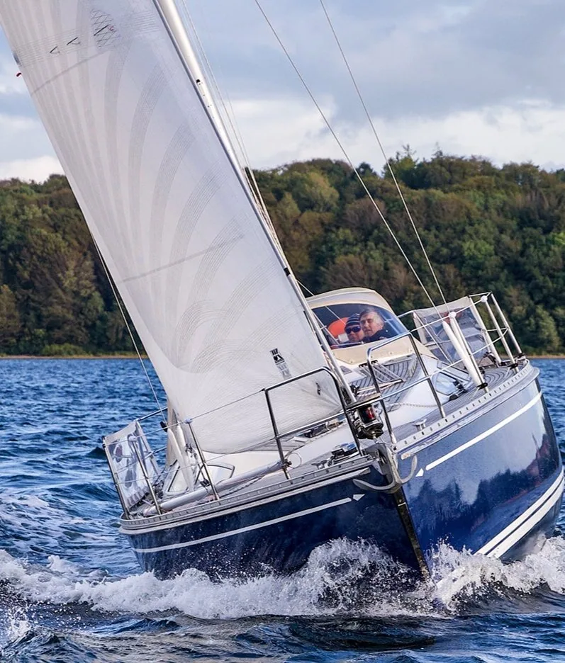 Bow-on view of the navy-hulled Comfortina 39 heeled under white X-Drive® Silver sails, two crew at the helm