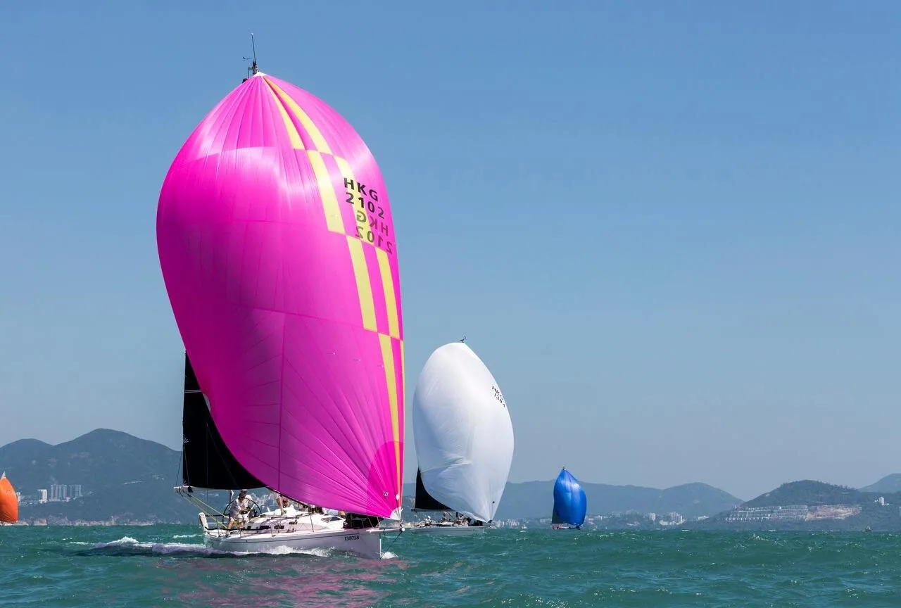 Racing fleet running downwind at the China Coast Regatta, led by a hot-pink spinnaker with yellow stripes