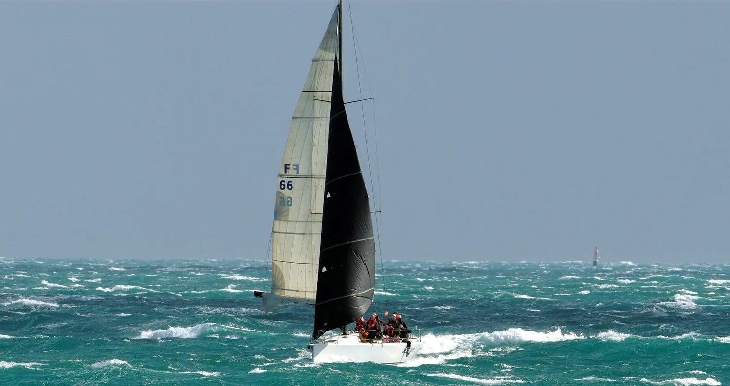 King 40 CHECKMATE running wing-on-wing in big seas, grey No. 4 genoa poled out and a reefed black mainsail