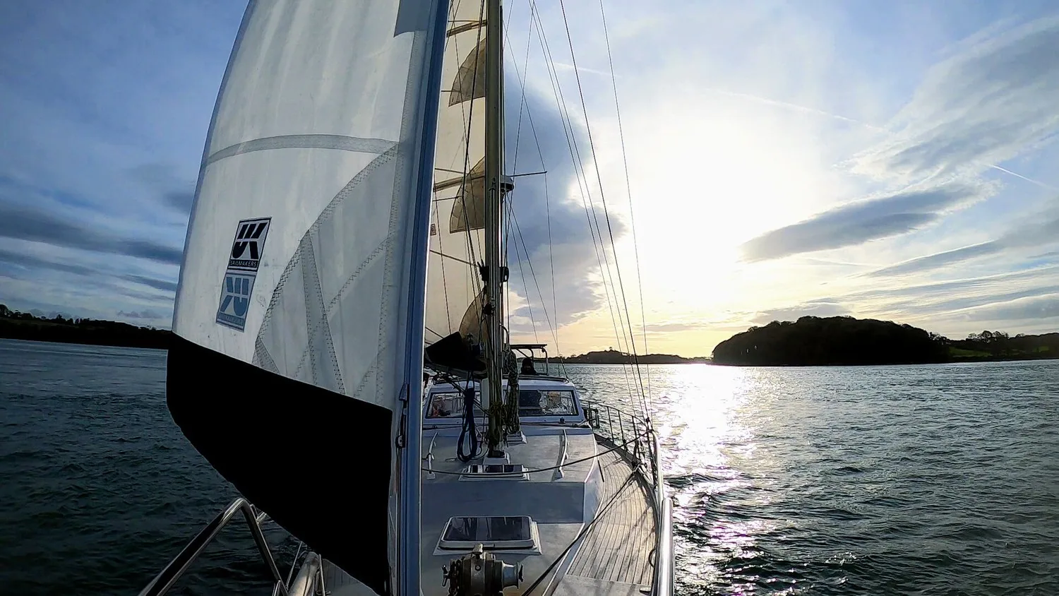 Looking forward past PANDA's white UK Sailmakers headsail towards a low island at sunset in Scotland